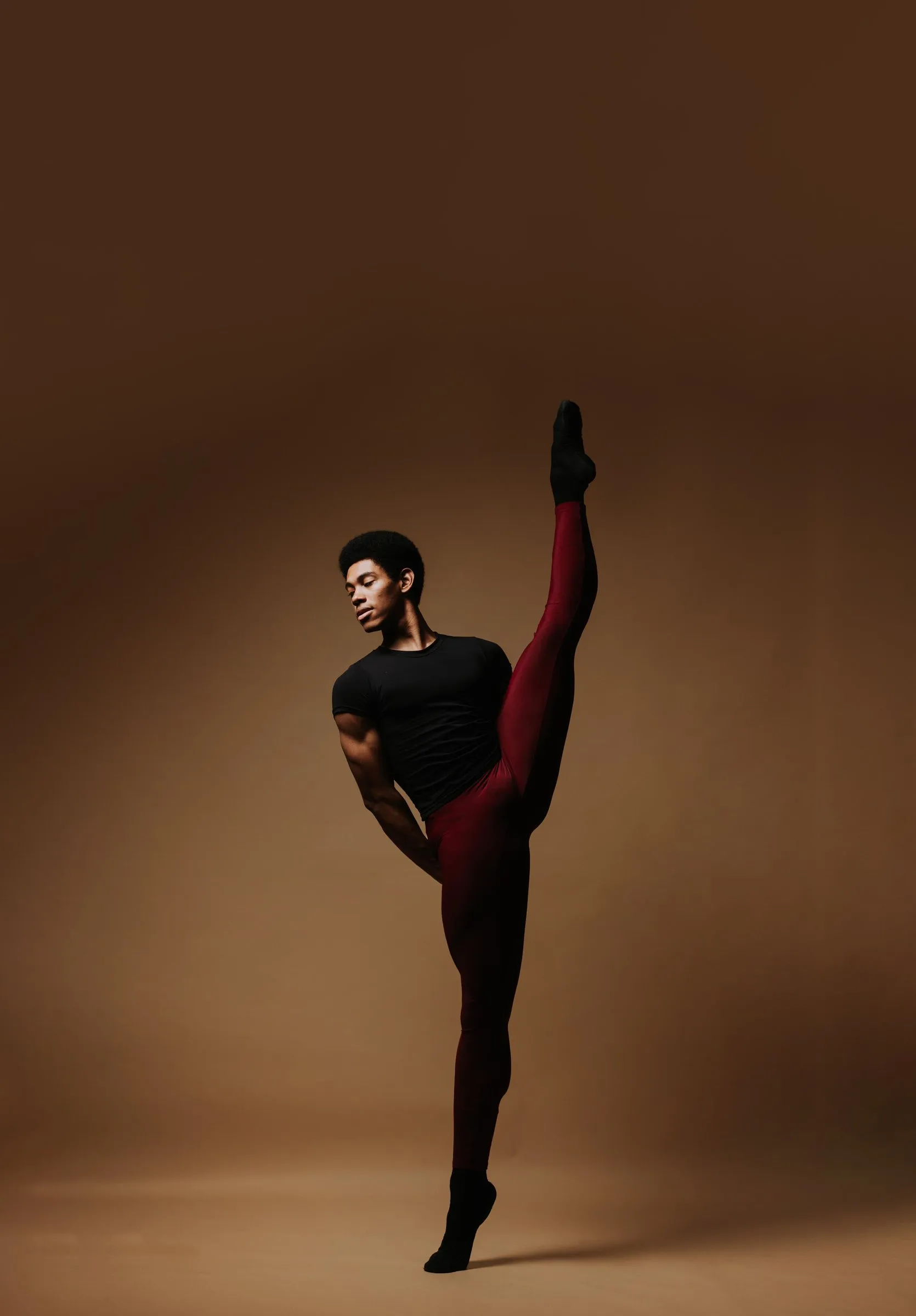 A male dancer in a high extension, holding his leg overhead